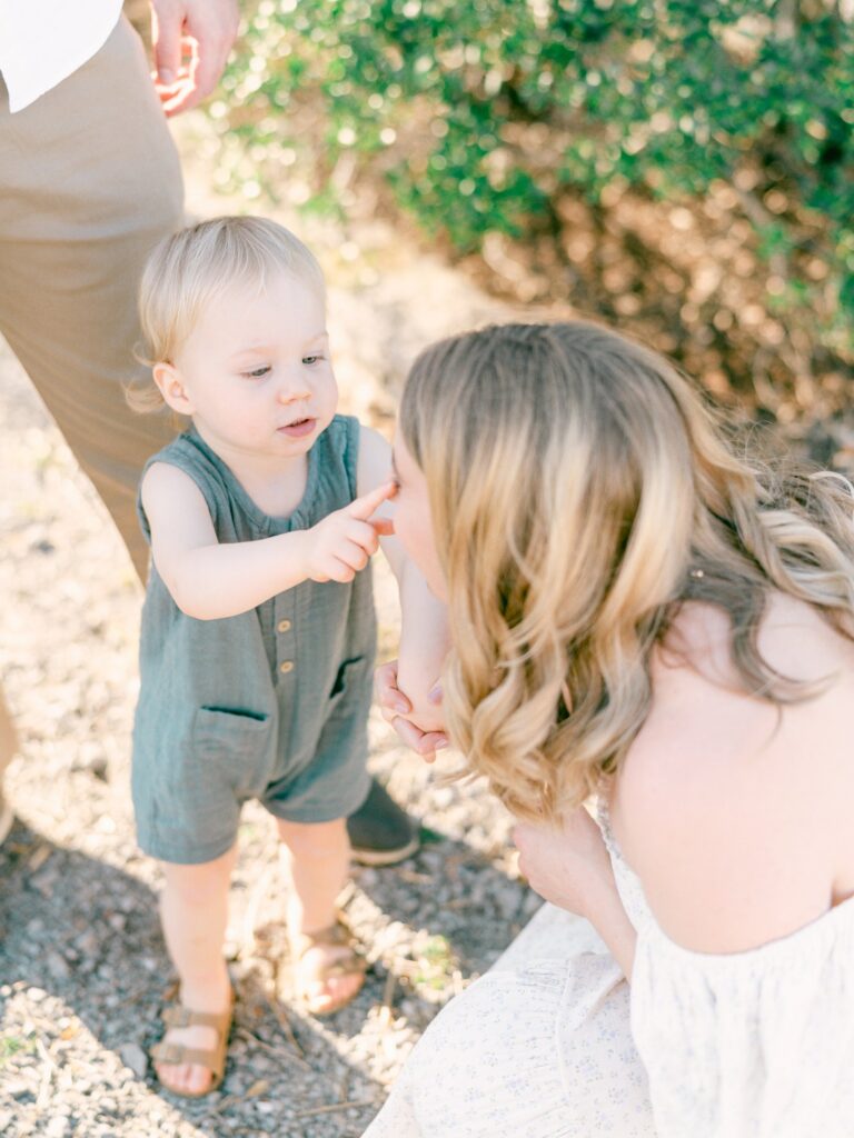 A toddler boy pokes his moms nose in a sweet candid photo during a maternity session