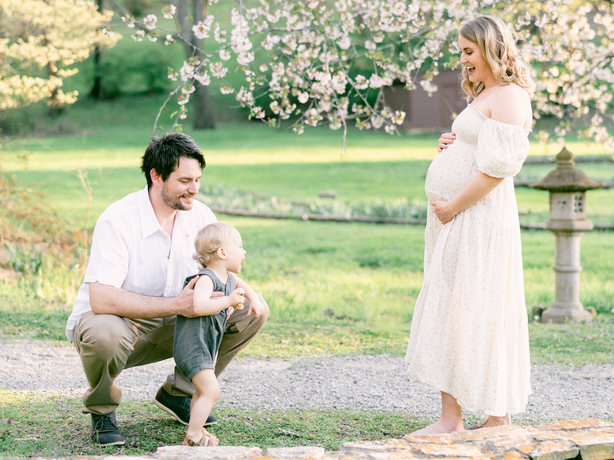 Franklin maternity photographer Courtney Houk captures dad squatting down and holding toddler, while standing mom with hands around her bump laugh down on them