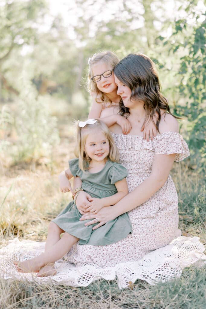 Mom with eyes closed as her two daughters snuggle up on her lap and around her neck