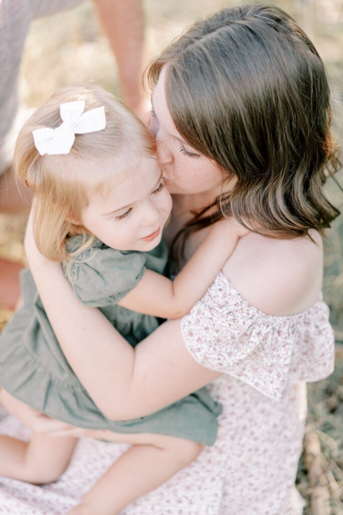 A mother kissing her youngest daughter on the cheek while they embrace in eachother's arms