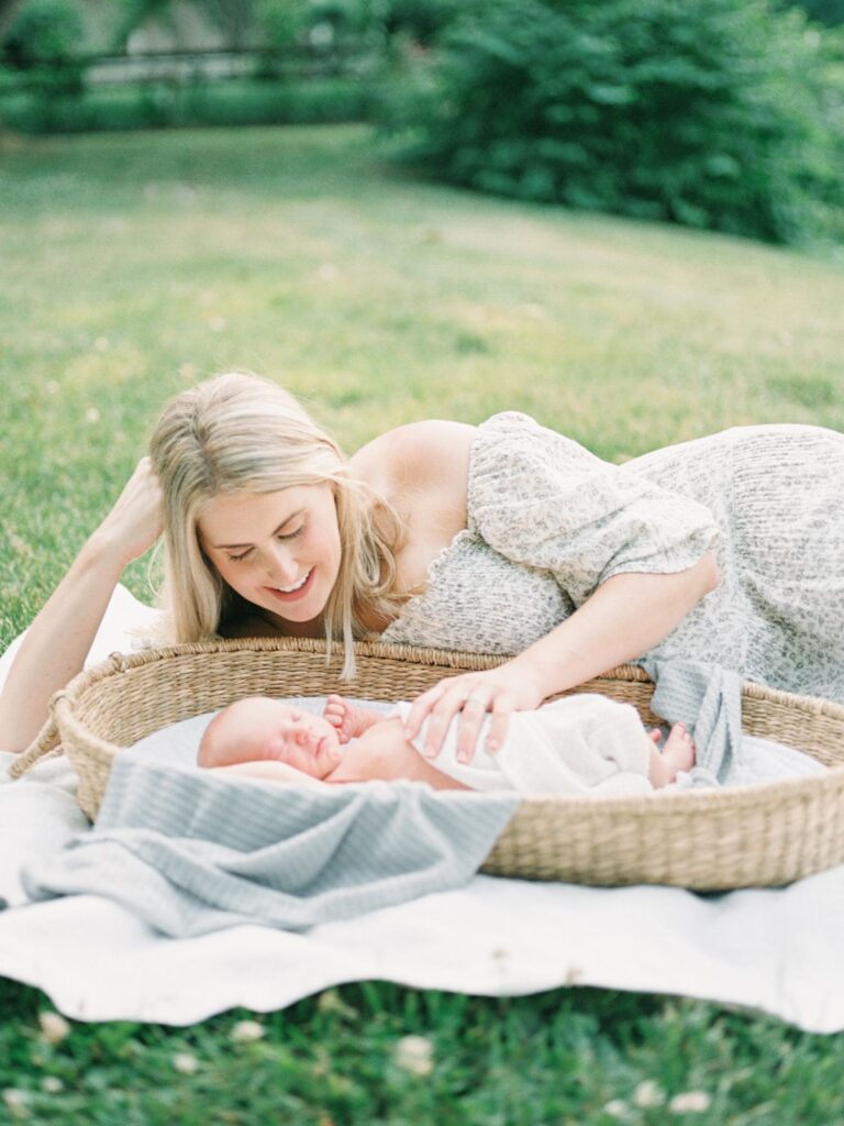 Mom admires newborn baby boy while laying in the grass together