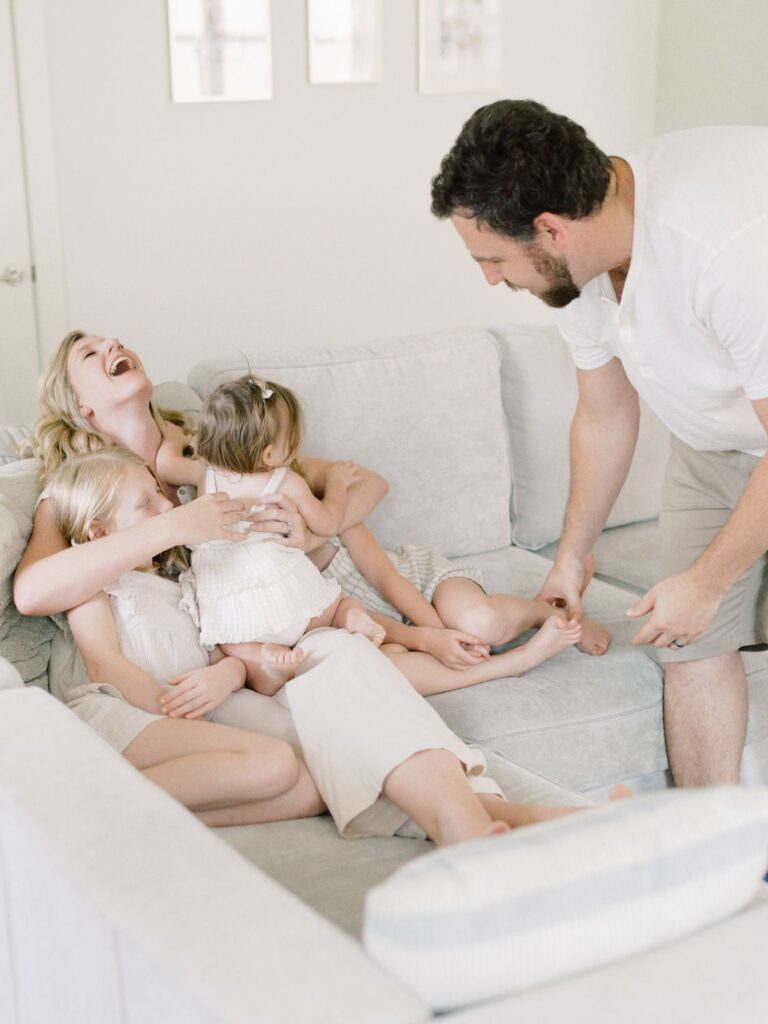 Mom laughs on cough while cuddling three daughters as dad goes to tickle daughter's feet
