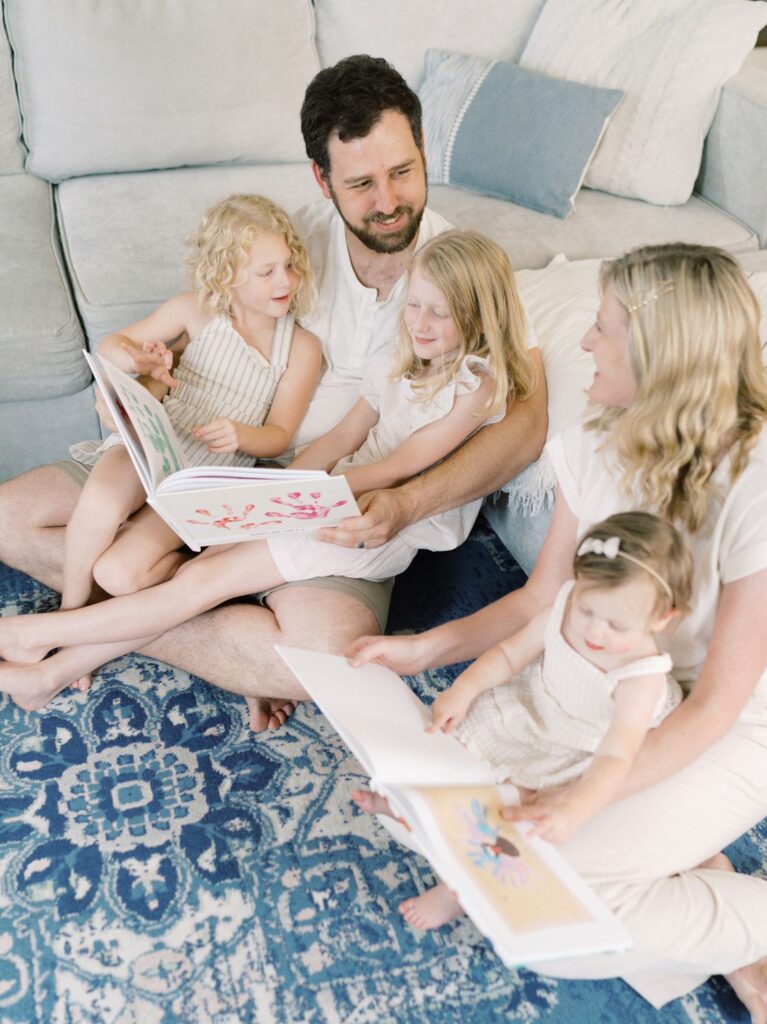 Mom, dad and three daughters reading books together on living room floor