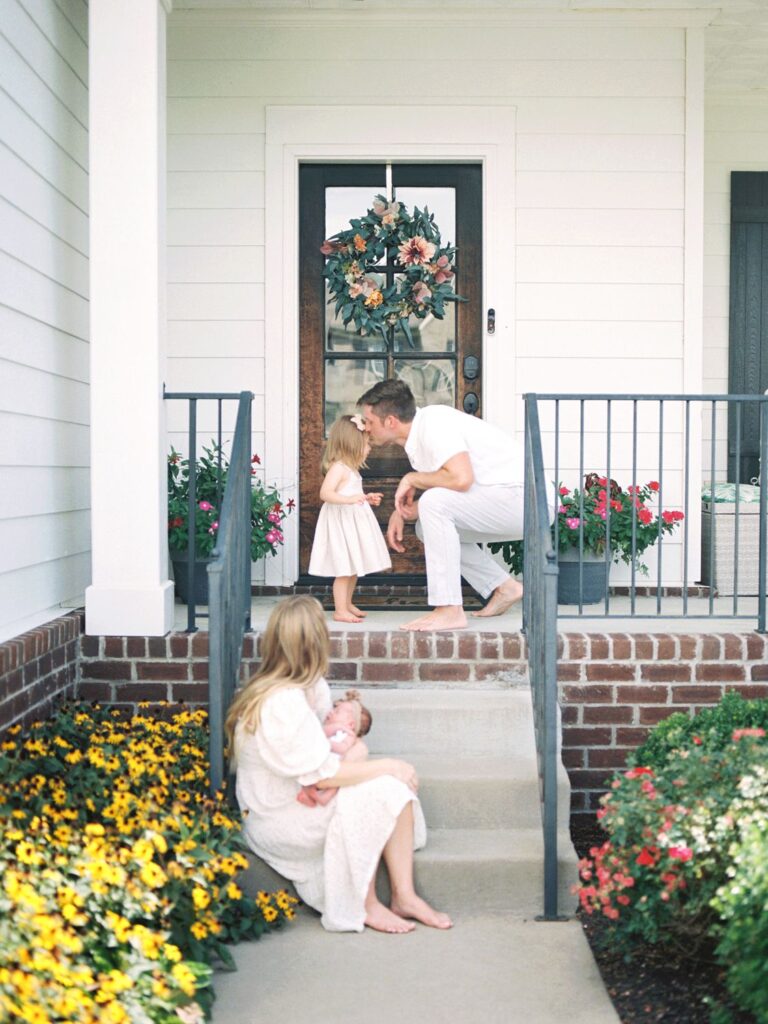 These in-home Nashville newborn photos by Courtney Houk Photography feature a mom, newborn baby, dad, and toddler on their front porch full of flowers
