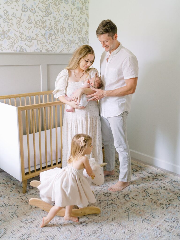 Mom and dad hold newborn baby girl while toddler sister plays on her rocking horse during these in-home Nashville newborn photos