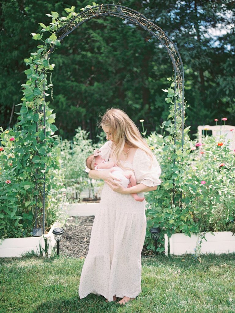 Mom holds newborn baby girl in backyard flower garden