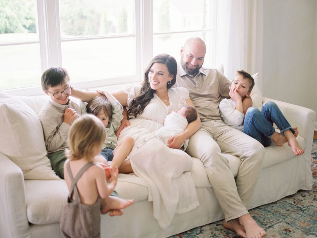 A new family of seven cuddle on the couch during these Nashville newborn photos with siblings as they welcome their baby brother