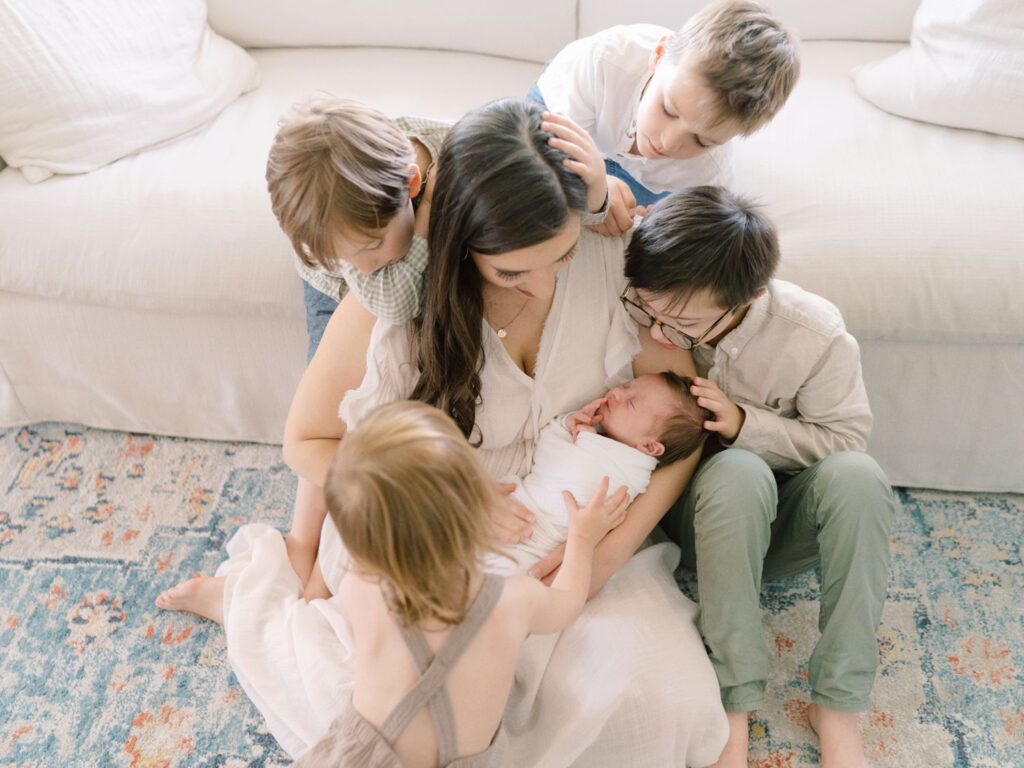 Photo captured by Franklin newborn photographer Courtney Houk of mom sitting on the ground cuddling her 5th baby boy while her four other boys surround her with love
