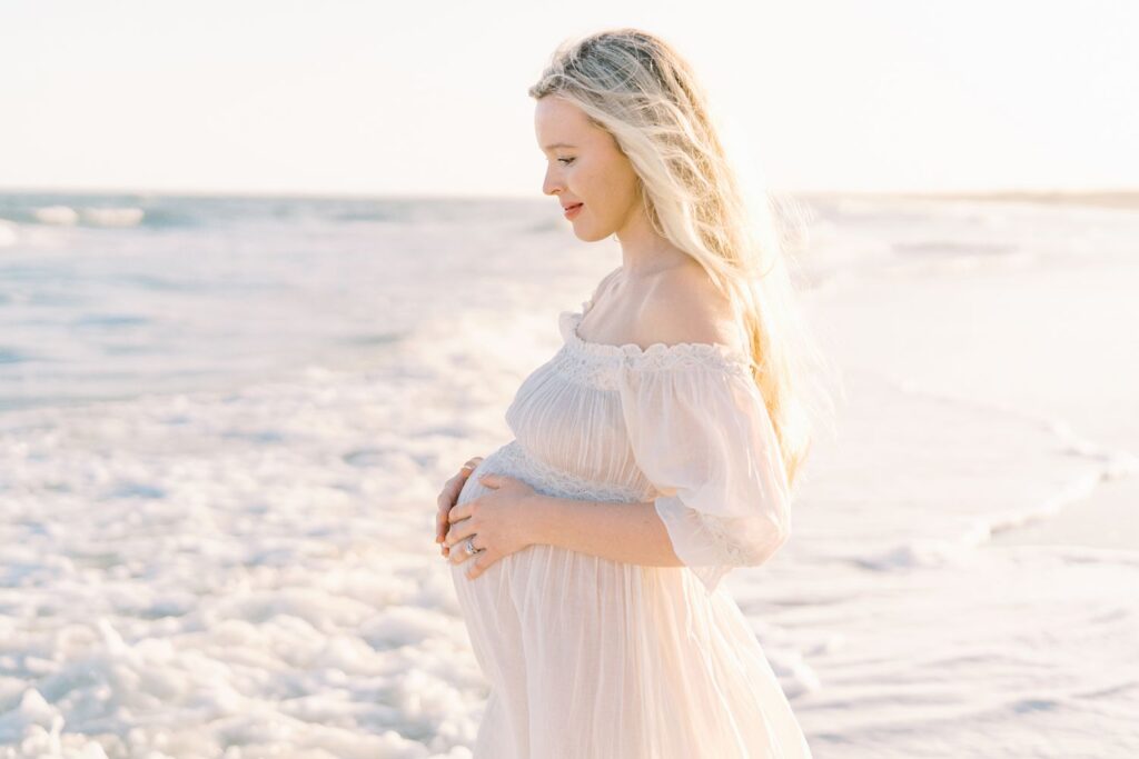 Pregnant mama standing in the waves of the ocean with her hands on her baby bump