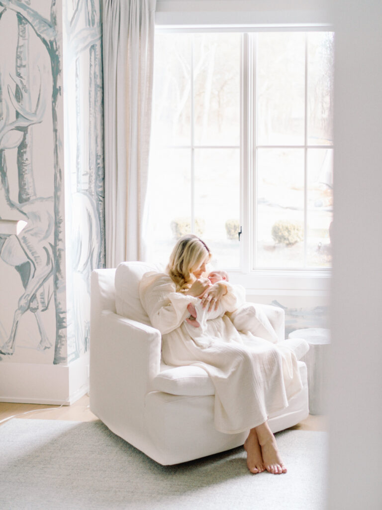 This photos captures a mom in a rocking chair holding her newborn baby boy