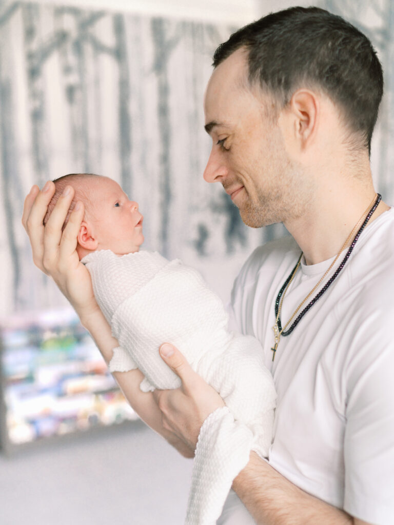 A new father holds his newborn baby boy close and smiles down at him