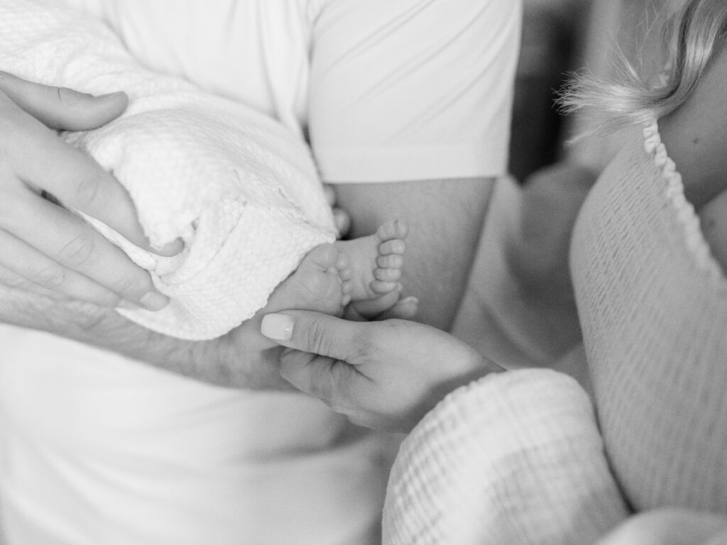 The black and white detail photo is on a dad cradling his son while his wife holds their baby boys toes