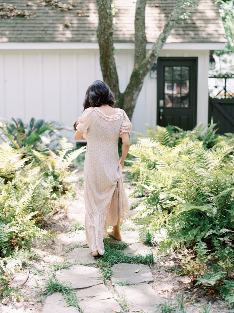 A mama walks away from the camera with her baby boy in one arm and her other arm holding her dress