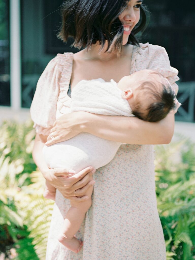 This close up image is of a mama cradling her 3 month old baby boy and she looks over her shoulder and smiles