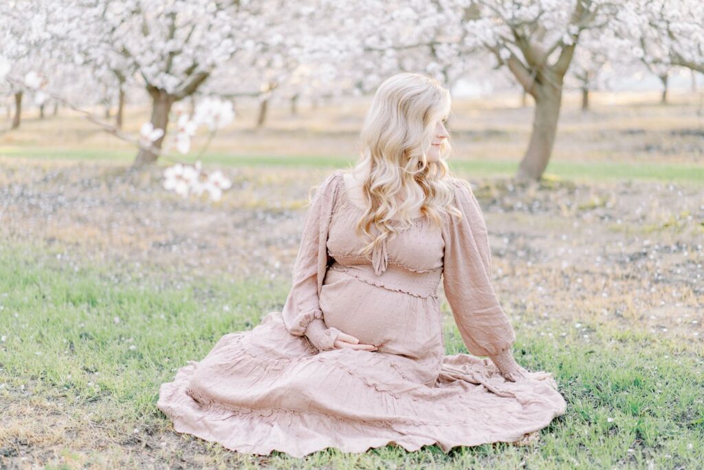 A pregnant mama sits in an open flower field with her hand on her bump