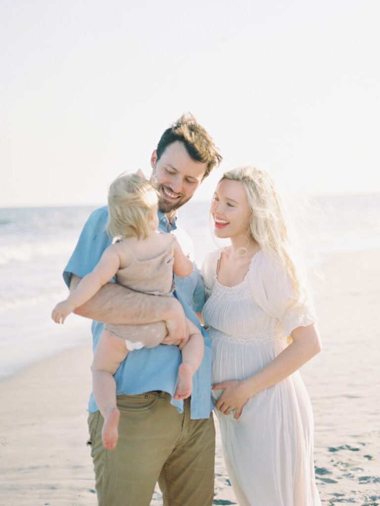 a mom and dad holding a baby on a beach