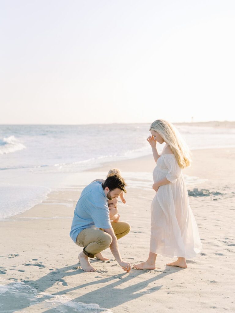 a man kneeling on the beach with a pregnant woman and a baby