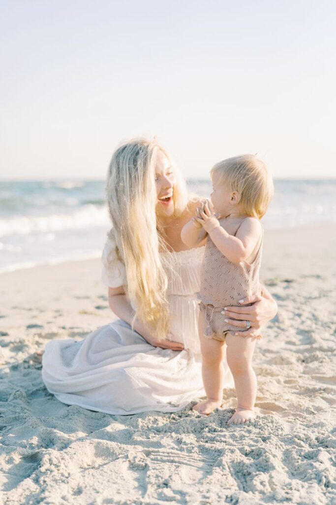 a pregnant mama and her one year old daughter on a beach playing in the sand