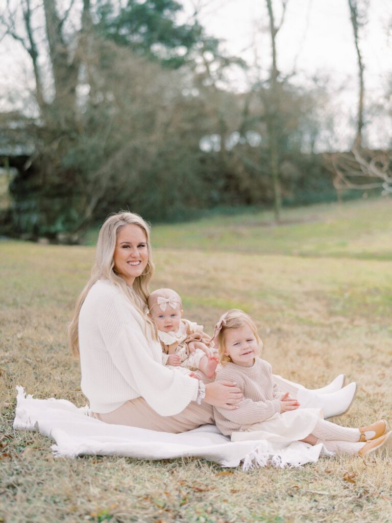 a mama and two daughters sitting on a blanket in the grass